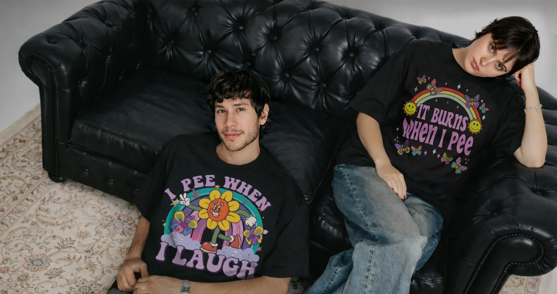 Two models wearing bold Y2K graphic tees on a black leather couch